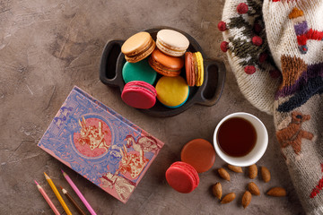 A cup tea with macarons and a notebook with colored pencils and a warm sweater. The concept of autumn or winter. Flat lay.