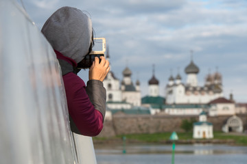 Tourist girl takes a photograph of the Spaso-Preobrazhensky Solovetsky Monastery from the deck of a ship