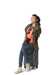 Fototapeta premium Excited happy Vietnamese young woman sitting on suitcase, isolated on white
