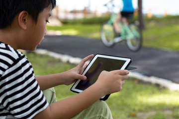 Asian little boy using digital taplet playing game at park