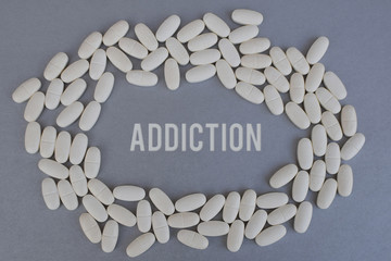 Circle of white medicine tablets or pills on silver color background with word addiction in middle. Pharmacy and healthcare concept.