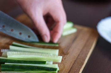 Woman?s Hands Cut Cucumber Matchsticks with Santoku Knife on a Wooden Chopping Board.  Salads, Maki and Temaki Sushi Rolls Ingredient.