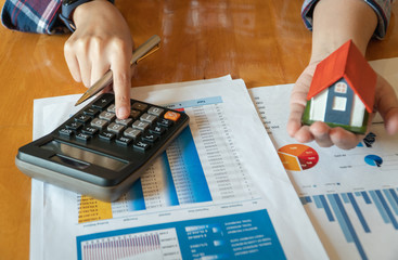 Woman holding house model in hand and calculating financial chart for investment to buying property.