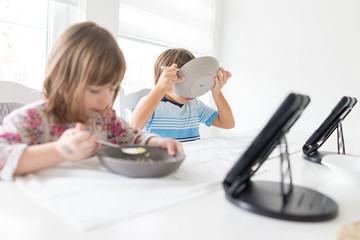 Kids in dining room eating and watching tablet