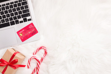 Laptop, credit card and candies on white fur background