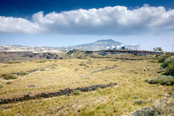 Fototapeta na wymiar Grass field and mountain against cloudy sky; Santorini; Greece