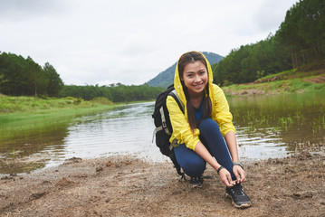 Beautiful female Vietnamese tourist tying shoe laces during short break by the river