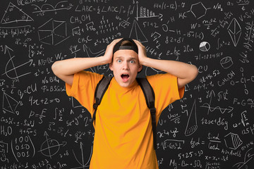 Shocked student standing by blackboard with math formulas - obrazy, fototapety, plakaty