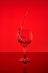 Splash of wine in a glass. Drink in glass on a red background.