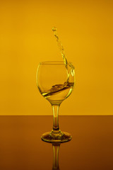 Splash of wine in a glass. Drink in glass on a yeallow background.