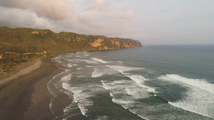 sandy beach parangtritis near ocean with big waves, people in tropical resort at sunset. Yogyakarta, Indonesia. aerial view seascape, ocean and beautiful beach. Travel concept. Indonesia, jawa