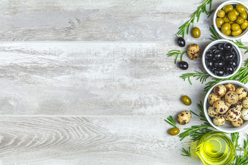 Fototapeta na wymiar Black and green olives, quail eggs on plates, olive oil and rosemary