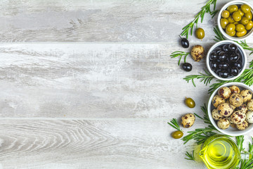 Black and green olives, quail eggs on plates, olive oil and rosemary
