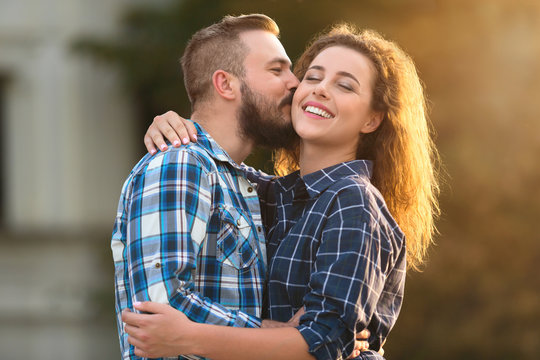 Handsome man kissing tenderly his girlfriend in cheek outdoors