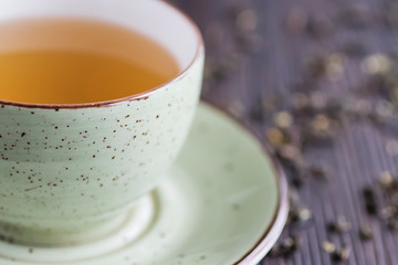 Cup of green tea and leaves of dry green tea on a brown wooden table. Superfood concept.