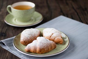 Freshly baked croissants cup with green tea on a brown wooden background.