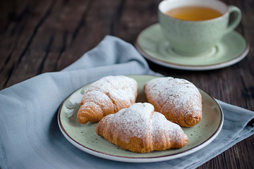 Freshly baked croissants cup with green tea on a brown wooden background.