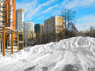 Russia, Moscow. Cityscape of courtyard of residental district in winter. Modern tall houses, clear day, blue sky. On sports ground is large snowdrift and tracks of tire on snow.