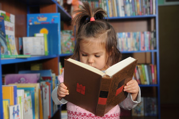Little girl reading book in library environment