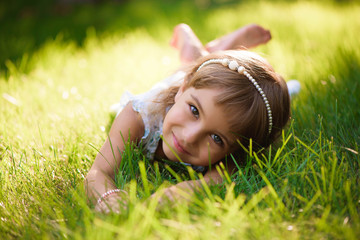 Cute little girl lies on grass in summer park