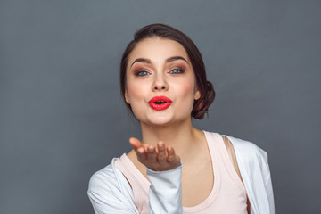 Freestyle. Woman standing isolated on grey sending kiss to camera excited close-up