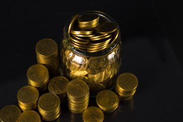 Coins stacks and gold coin money in the glass jar on dark background, for saving for the future banking finance concept.