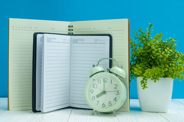 Office supplies or office work essential tools items on wooden desk in workplace, notebook, alarm clock and little tree with blue wall background.