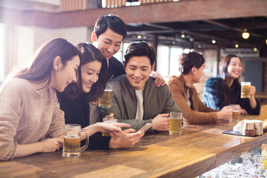 Happy friends using smartphone in bar