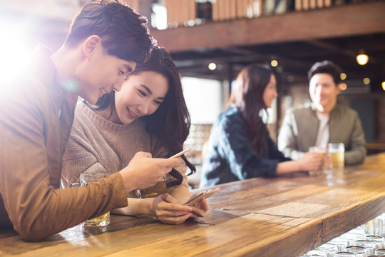 Happy friends using smartphone in bar