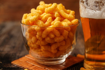Crispy peanut puffs or flips snacks and cup of beer. Close-up on rustic vintage wooden table.