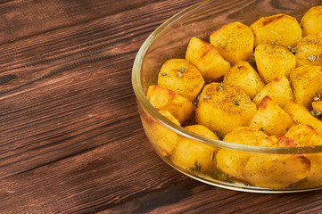 Naklejka na ściany i meble Baked Spiced Potatoes in cookware on a brown wooden bakground, close-up