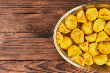 Baked Spiced Potatoes in cookware on a brown wooden bakground, falt lay