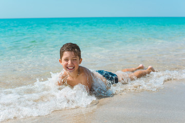 A cheerful kid on the beach lies in the clear sea water.