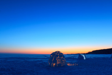 A snowy house called an igloo at sunset.