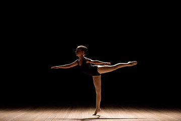 Cute little ballerina in dark ballet costume dancing on the stage. Kid in dance class. Child girl is studying ballet. © nagaets