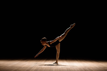 Cute little ballerina in dark ballet costume dancing on the stage. Kid in dance class. Child girl is studying ballet.