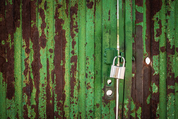 Puerta verde  de metal oxidada, cerrada con candado.