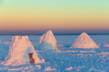The camp consists of several snowy houses called an igloo in the rays of the setting sun. - Powered by Adobe