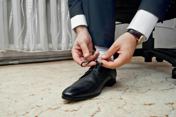 Fototapeta premium The bridegroom is dressed for a wedding ceremony. Hands and shoes close-up.