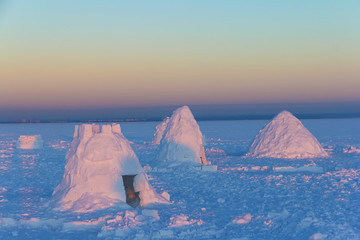 The camp consists of several snowy houses called an igloo in the rays of the setting sun.