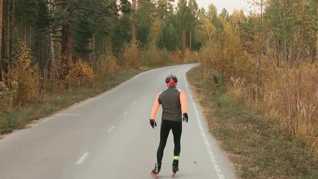 Training an athlete on the roller skaters. Biathlon ride on the roller skis with ski poles, in the helmet. Autumn workout. Roller sport. Adult man riding on skates. Shooting an athlete in motion a