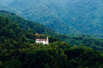 Fototapeta na wymiar Catholic church outstanding alone in the forest green hills of Toscany, Italy
