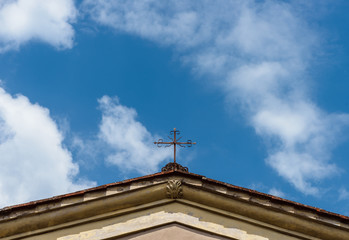 A cross on the roof of a catholic church in Italy on the background of blue sky with white clouds
