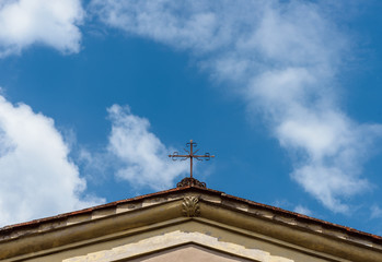 Obraz premium A cross on the roof of a catholic church in Italy on the background of blue sky with white clouds