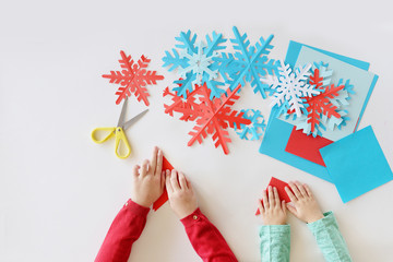 Children's hands cut out on a white background blue and red snowflakes from paper