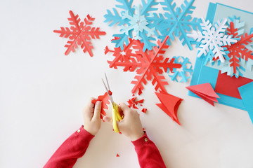 Children's hands cut out on a white background blue and red snowflakes from paper