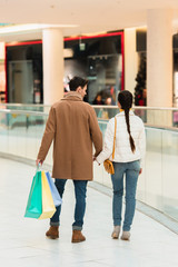 back view of loving couple with shopping bags holding hands in mall