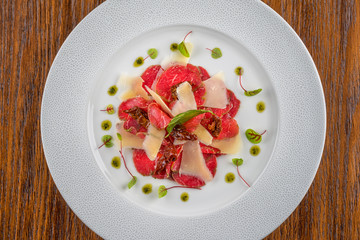 exclusive carpaccio of beef fillet served on white plate with parmesan, pesto and herbs, product photography for modern gastronomy