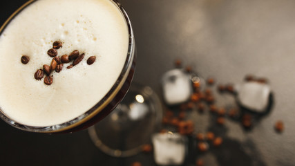 Glass with coffee drink, white crema, coffee beans, black background, ice cubes. Close up. Top view