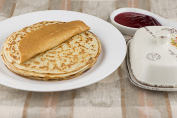 the celebration of carnival: fresh cooked real Russian pancakes made with yogurt, on a white plate, shrovetide and currant jam. Linen tablecloth, front view, close